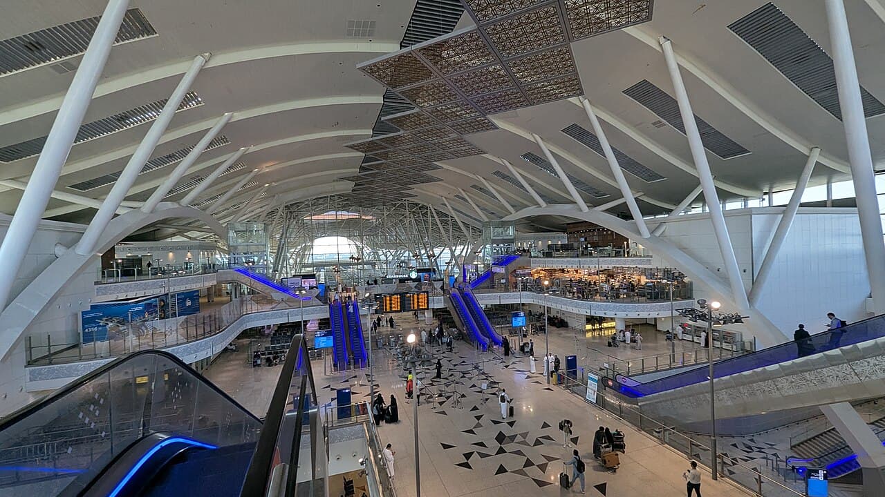 Interior of Jeddah Airport Haramain station with escalators and a departures board.