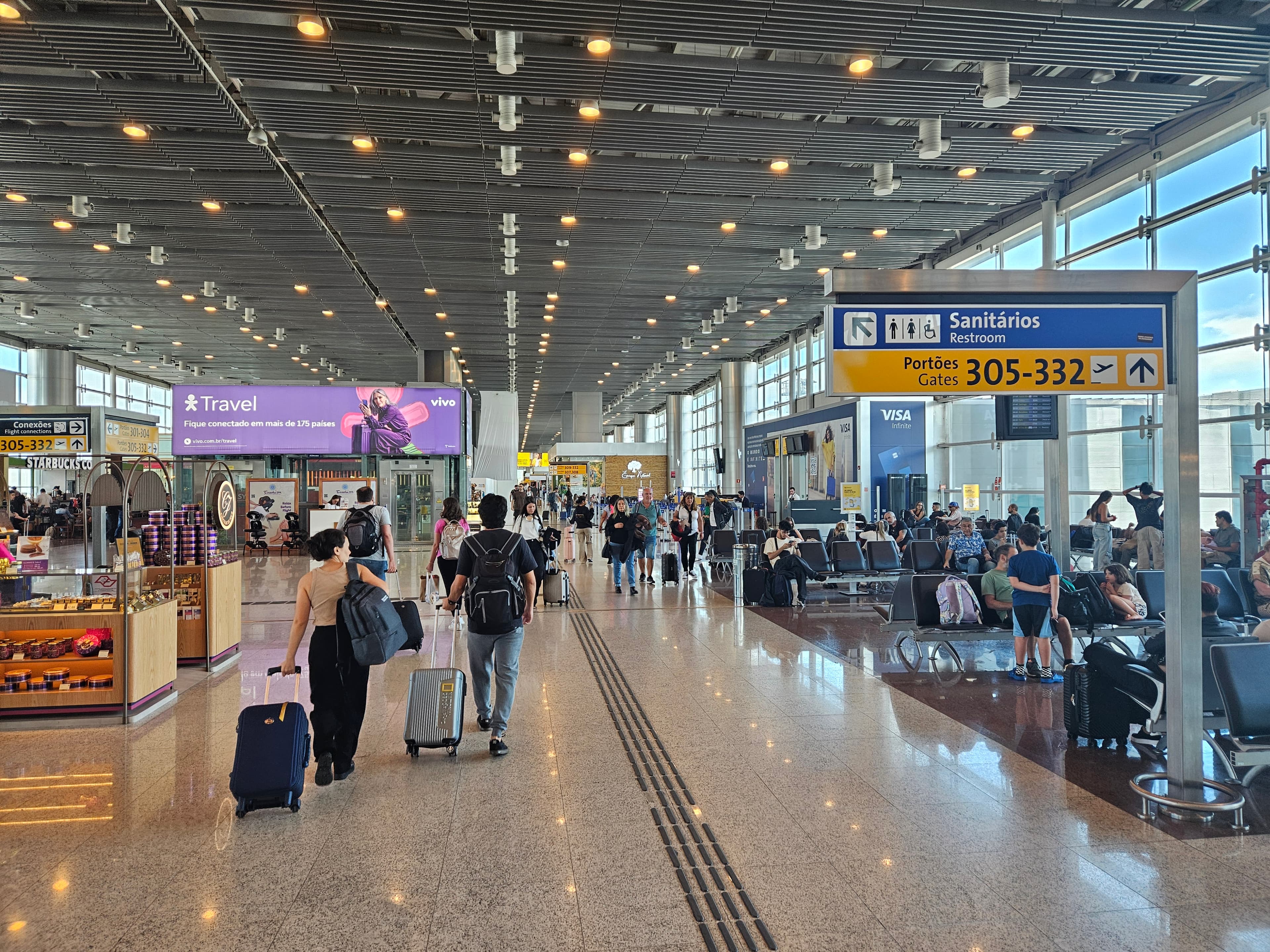 Passengers and yellow gate-direction signs in Guarulhos Airport Terminal 3