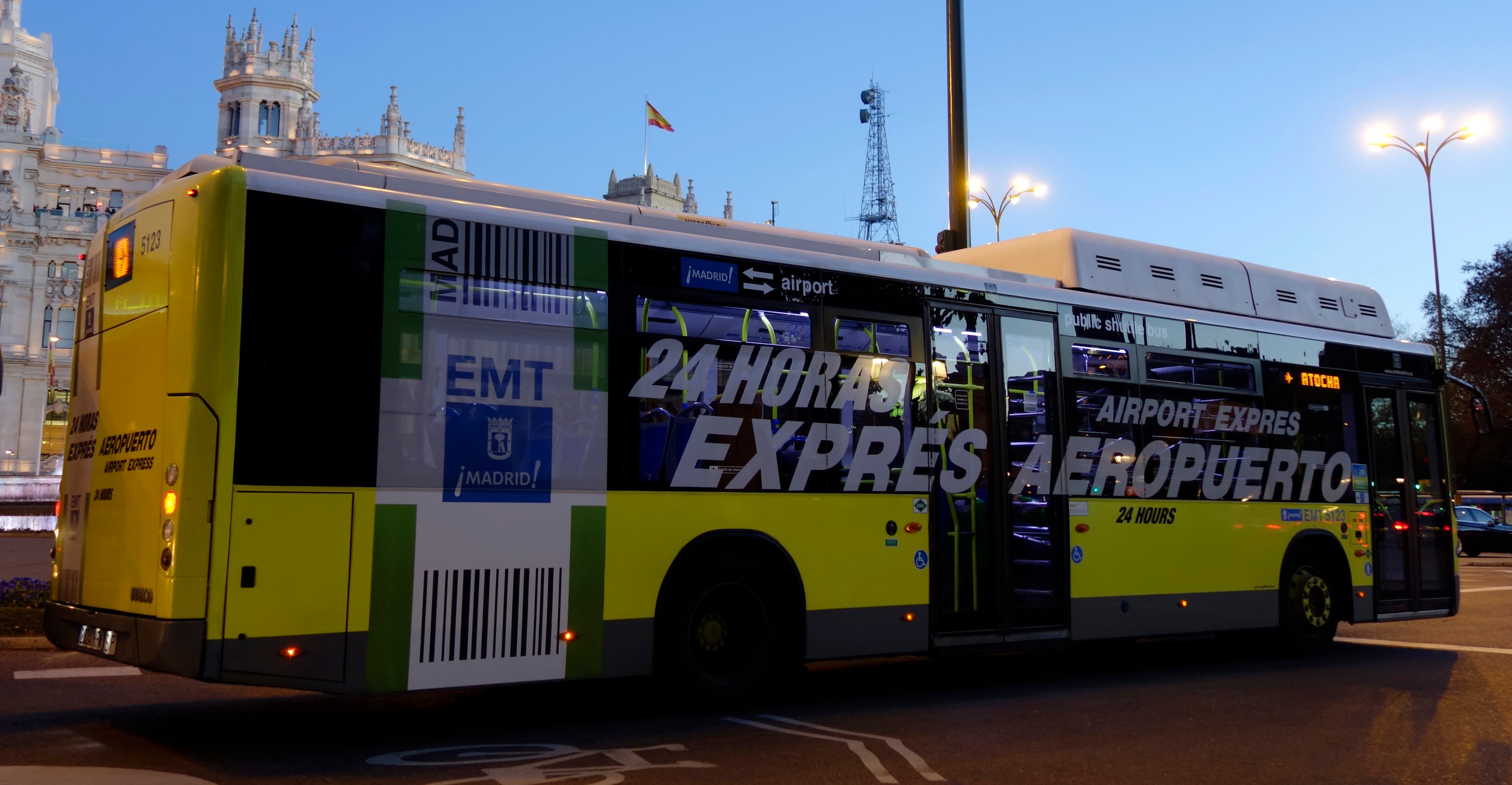 Yellow Airport Express bus beside the illuminated Palacio de Cibeles in Madrid