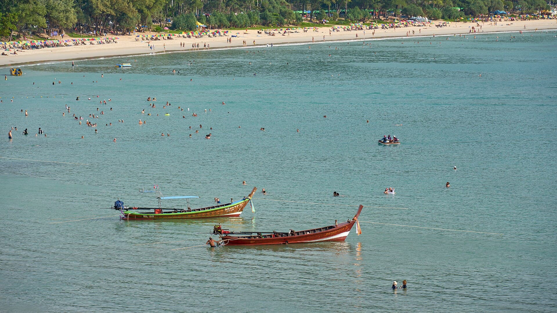 Longtail boats on clear turquoise water at Kata Beach, Phuket.