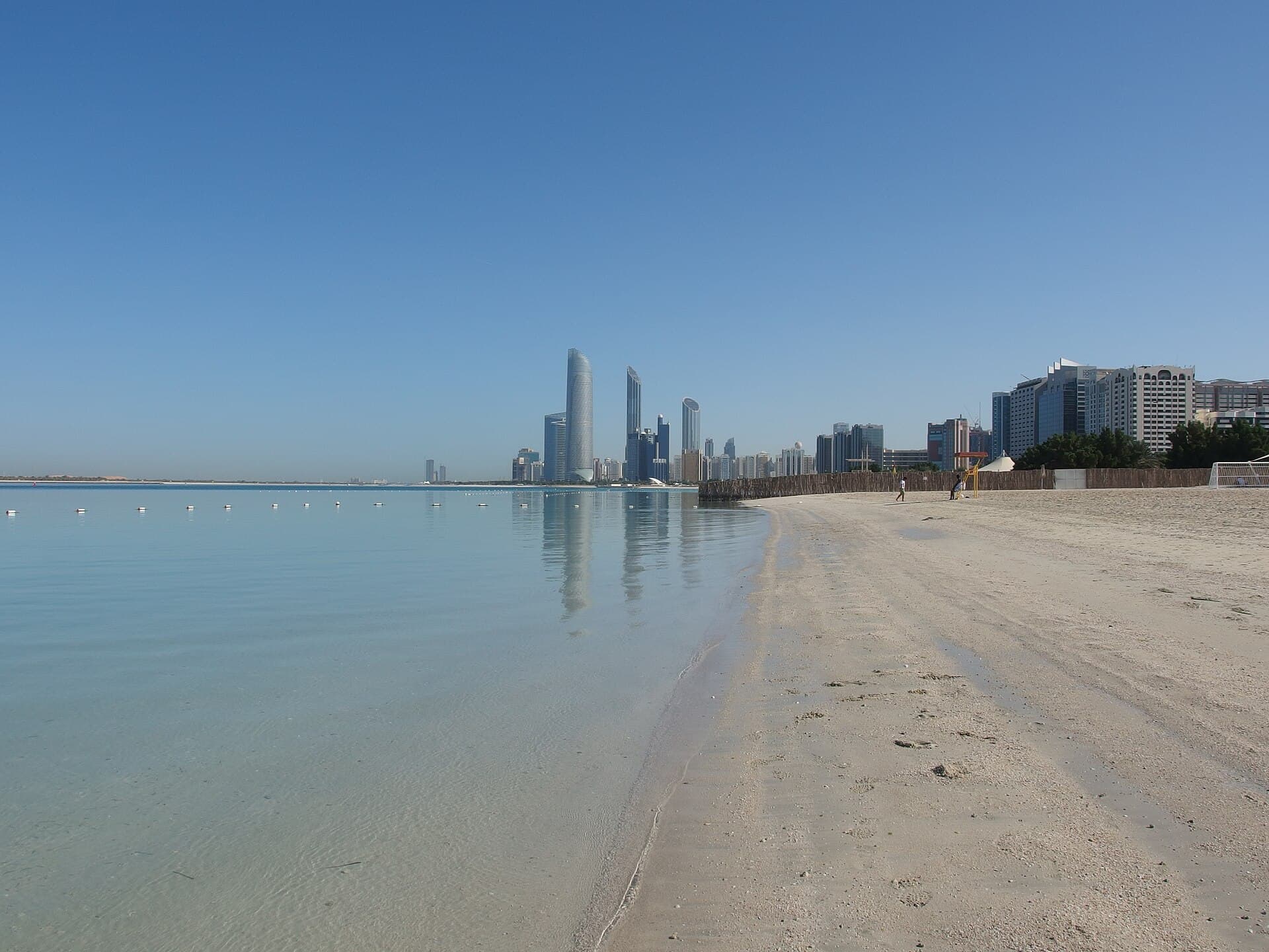 Calm turquoise water and sand on Abu Dhabi’s Corniche, with the city skyline in the distance.