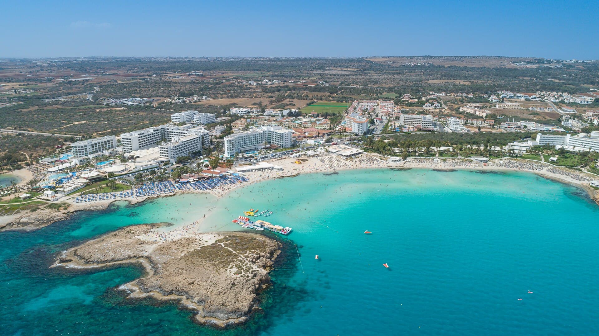 Aerial view of Nissi Beach’s turquoise bay, pale sand and small island in Ayia Napa.
