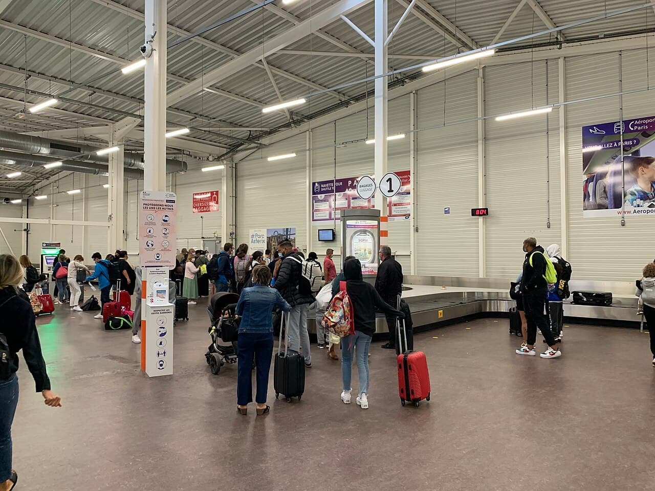 Passengers with luggage beside a baggage carousel at Beauvais–Tillé Airport.