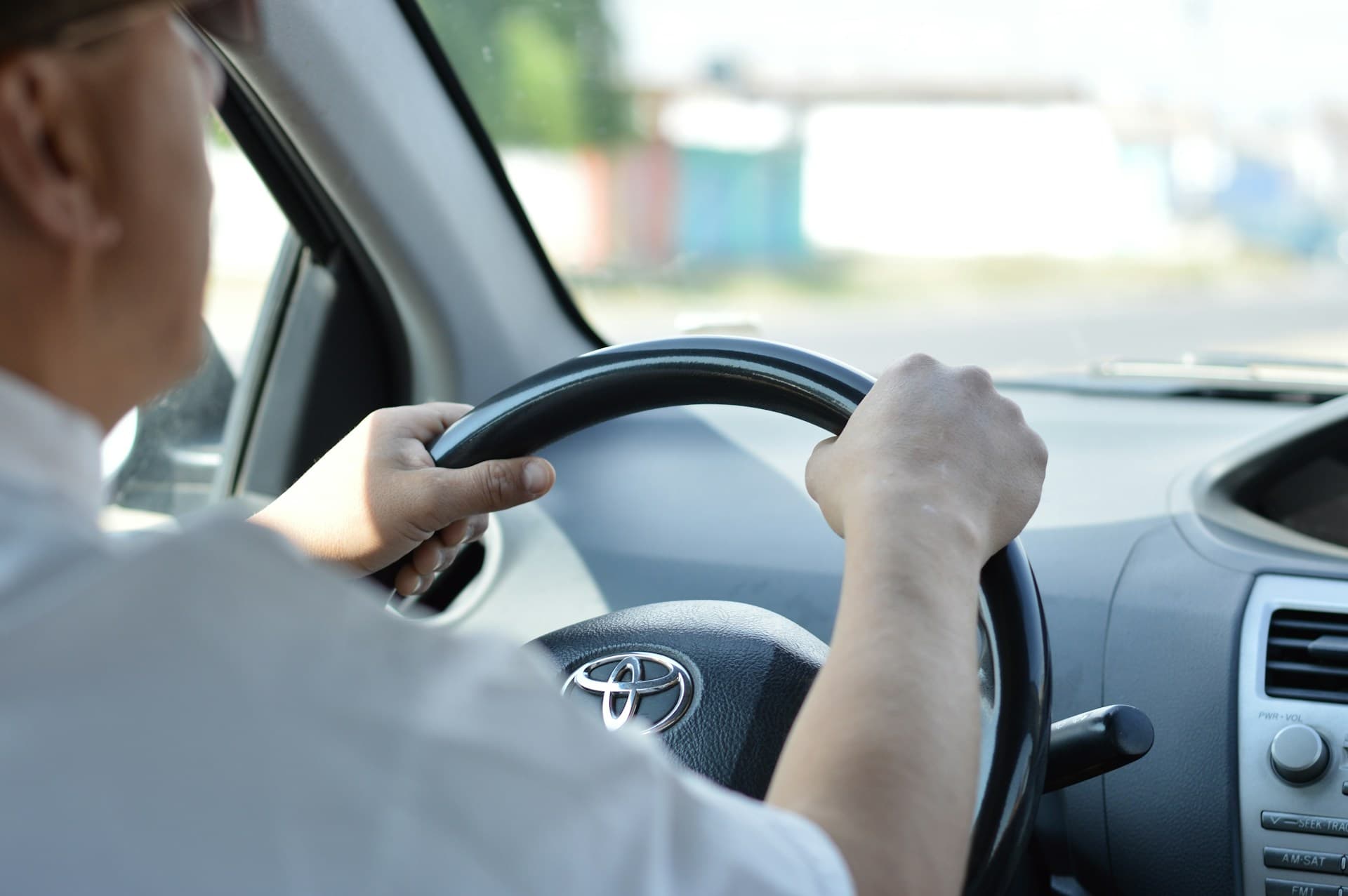 A driver in a white shirt holding the steering wheel with both hands in daylight.
