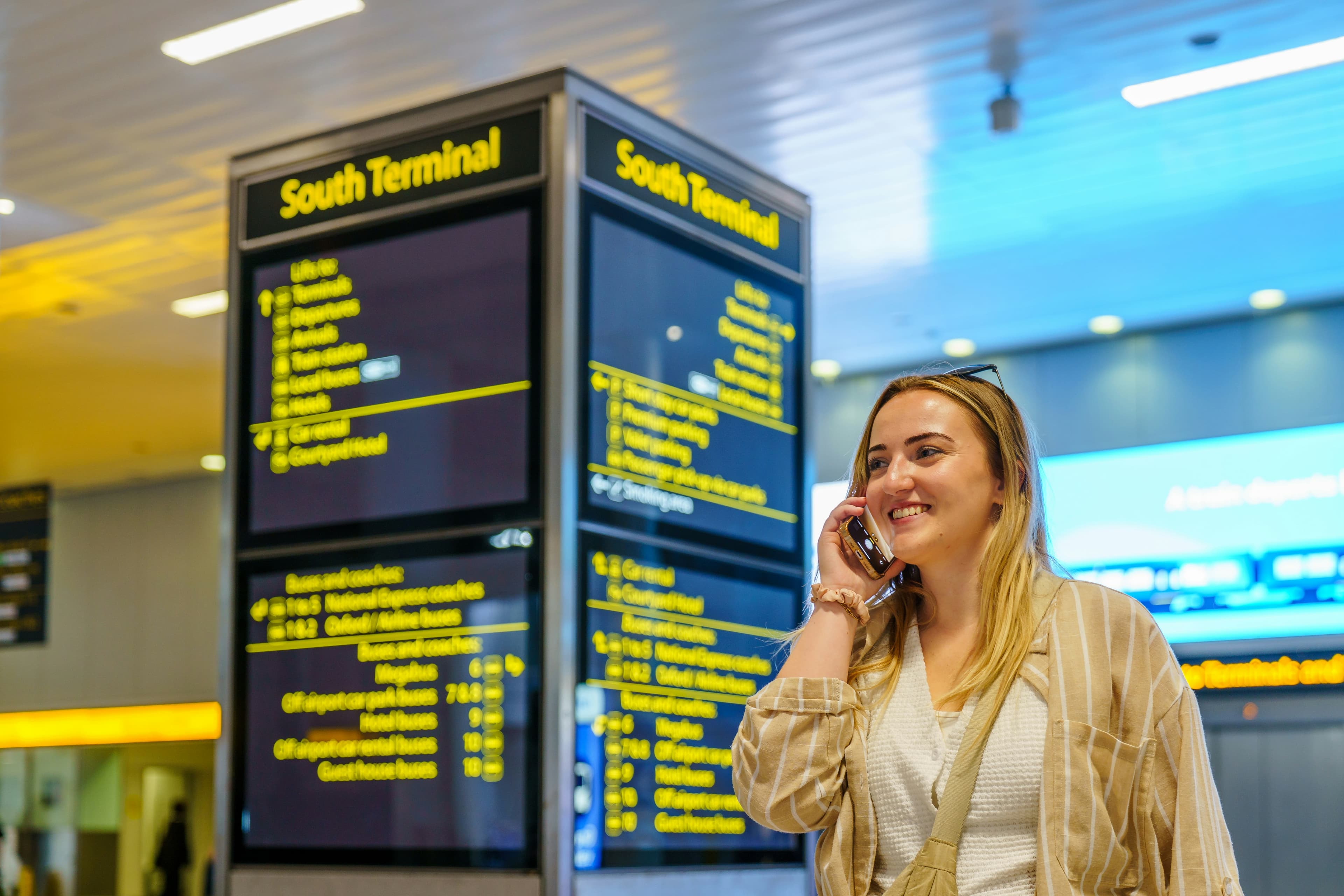 A woman speaking on her phone beside a South Terminal sign at Gatwick Airport.