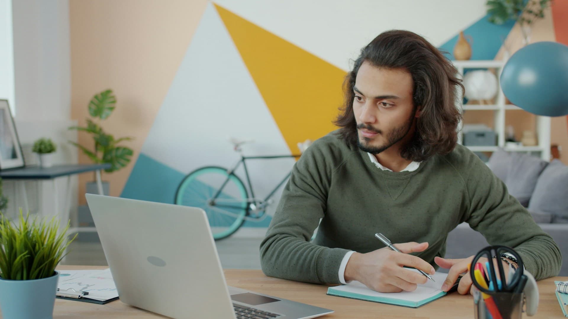 A man looking at a laptop while writing notes in a notebook.