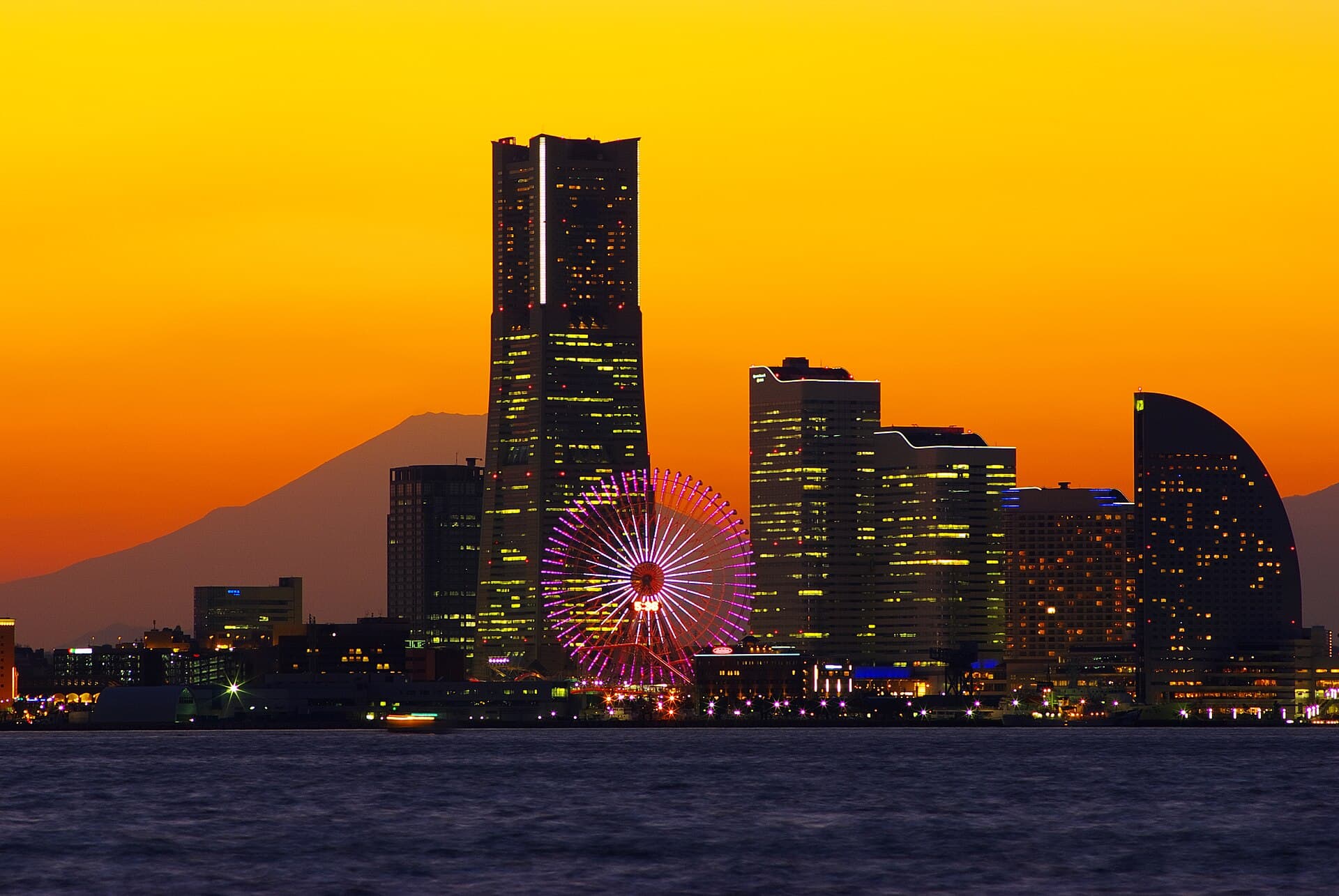 Yokohama’s Minato Mirai skyline and illuminated Ferris wheel against an orange sunset, with Mount Fuji behind.