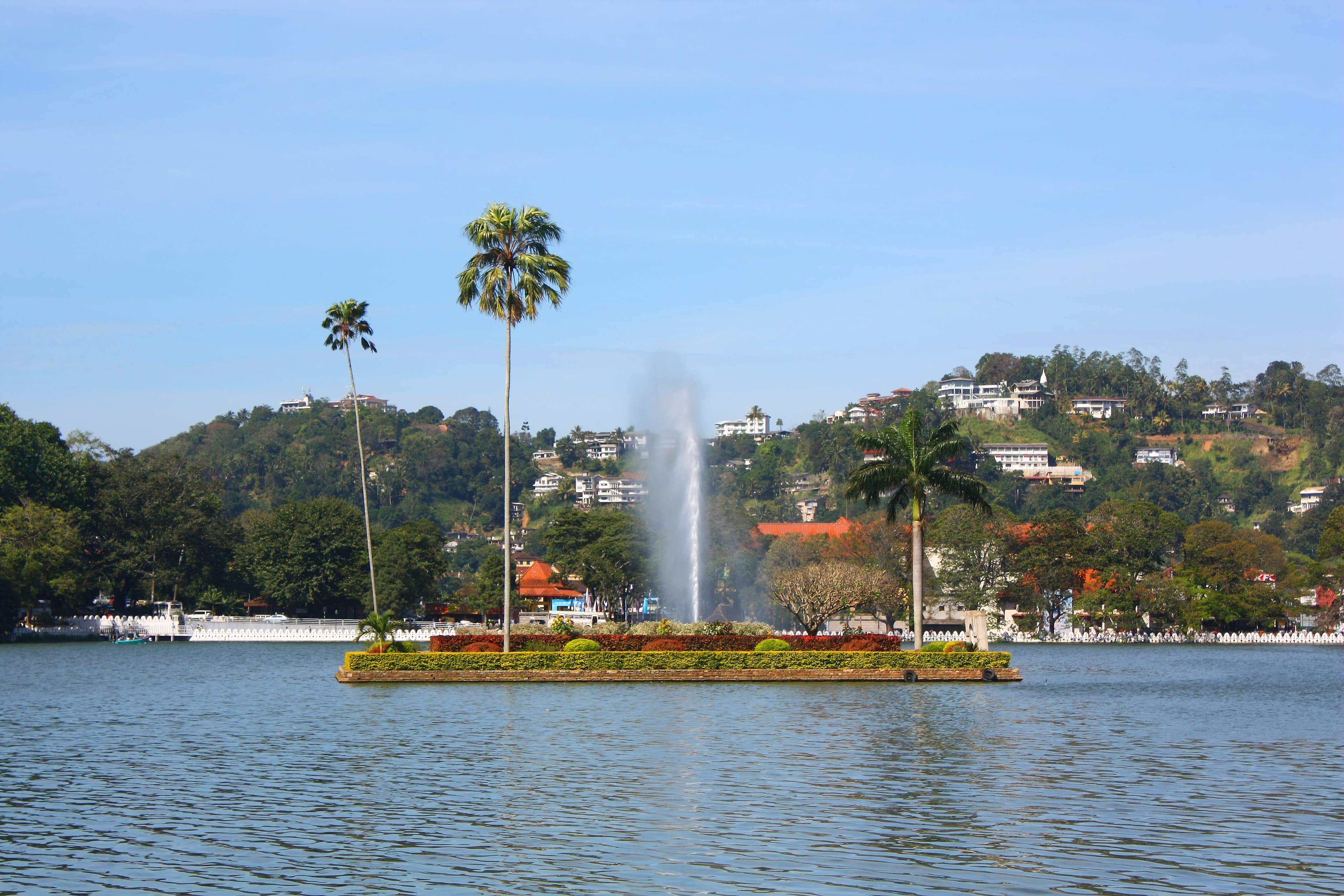 Island and fountain on Kandy Lake, with palms and green hills behind