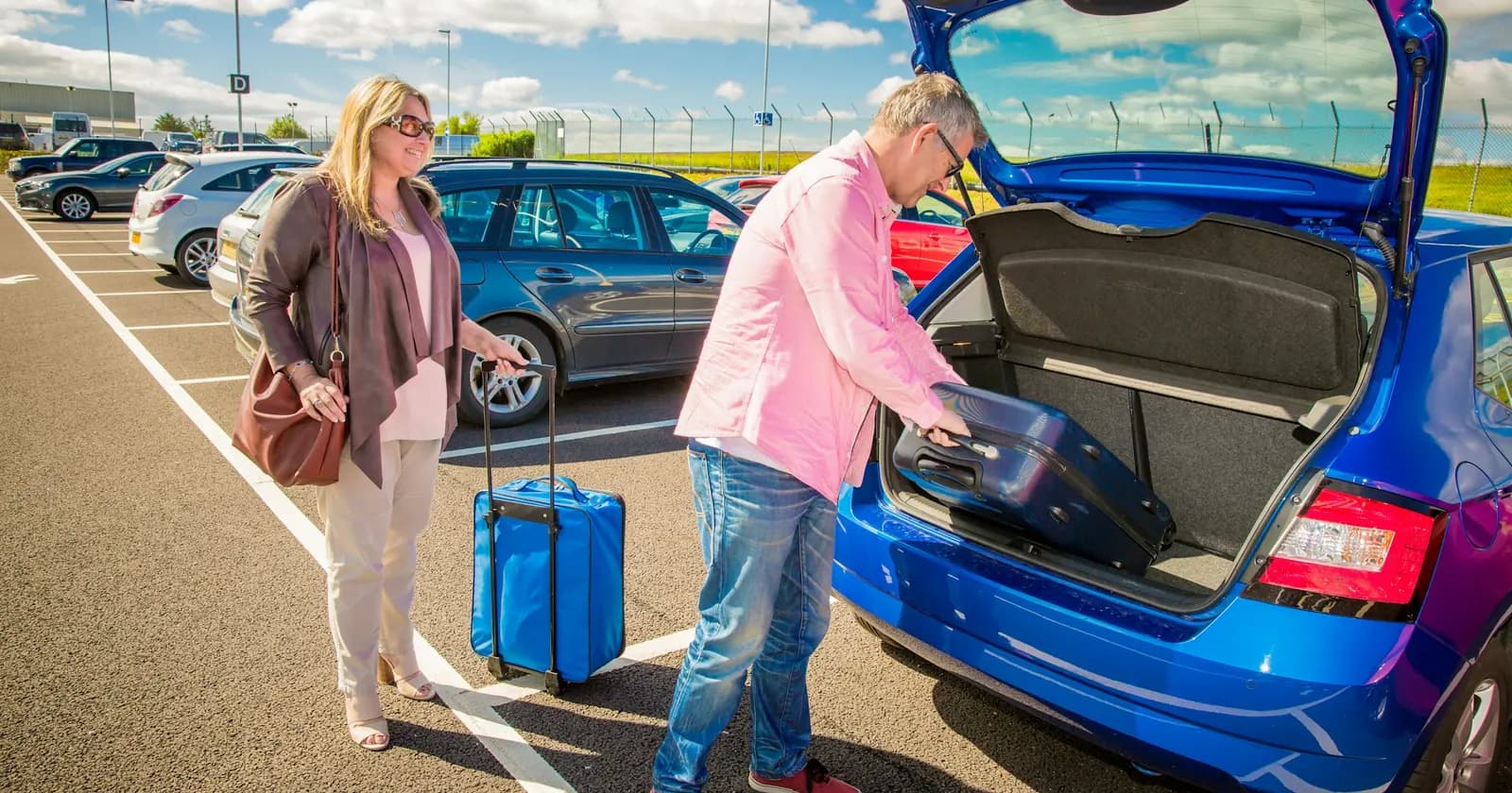 Two travellers loading a suitcase into a blue car