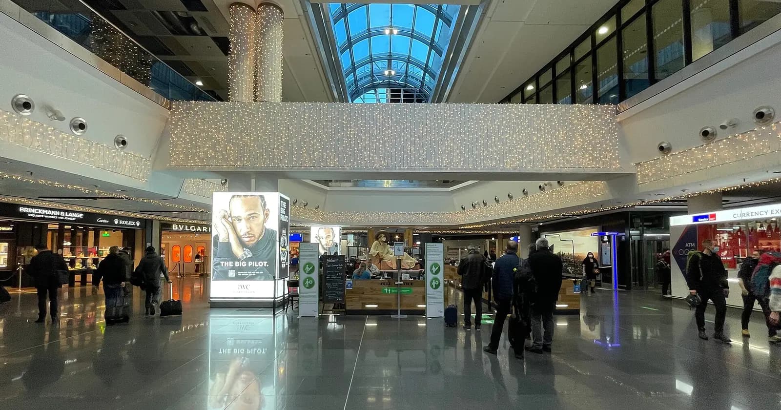 Travellers beneath a blue glass roof in Frankfurt Airport Terminal 1